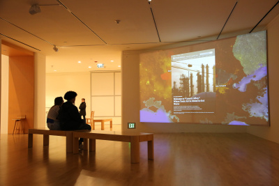 two visitors siting on a bench looking at a projected screen