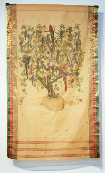An abstract tree filled with birds and fruit is on yellow rectangular fabric. The tree takes up 2/3 of the space with bands along its borders. These bands frame the tree and are lighter weight than the thick green and red borders on the left and right of the tree. 