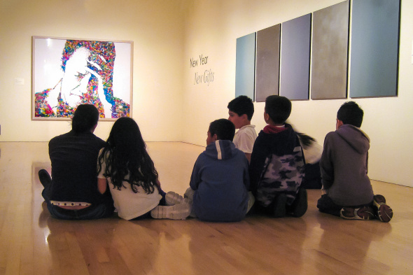 Group of children sitting on the floor in a museum gallery, observing colorful and monochromatic artworks during a self-guided tour.