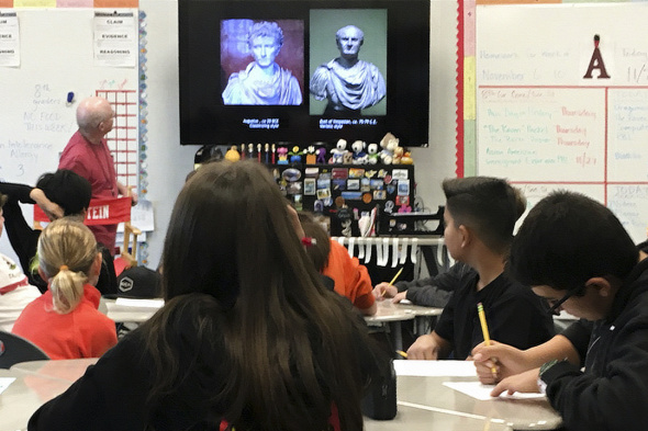 Teacher presenting images of classical sculpture to students in a classroom.
