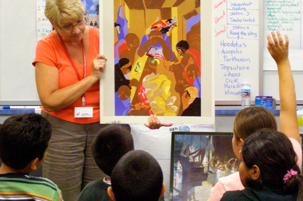 Teacher presenting an artwork reproduction to students in a classroom.
